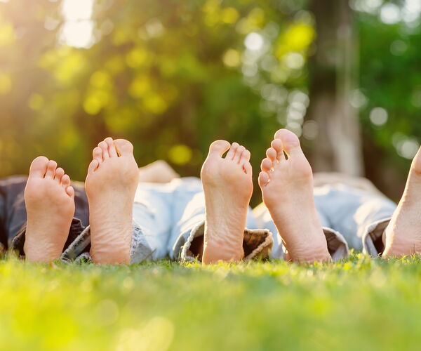 Five bare feet lie on green grass, the toes visible. The feet belong to people lying in a row.