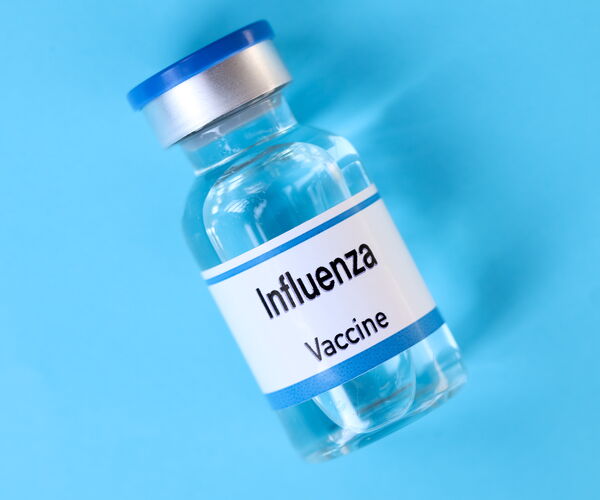 Transparent vaccine container with silver closure and blue cap. The label reads ‘Influenza Vaccine’.
